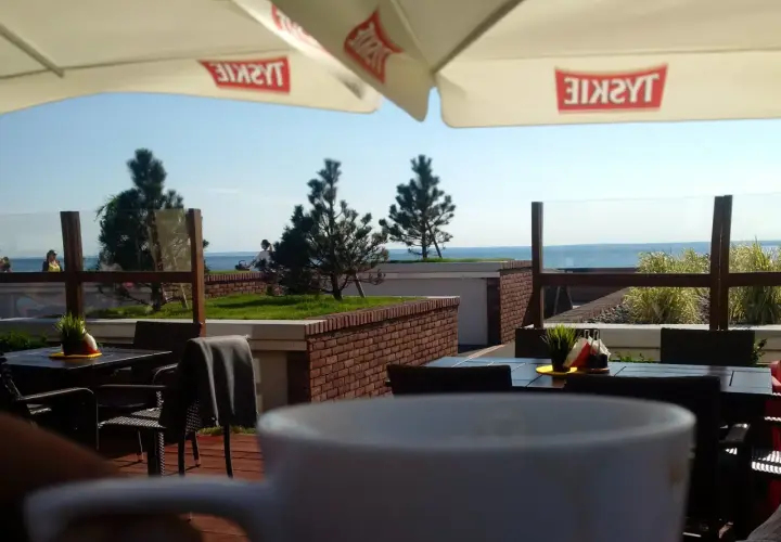 Widok z kawiarni na plaży z widokiem na morze i parasolami z logo Tyskie.