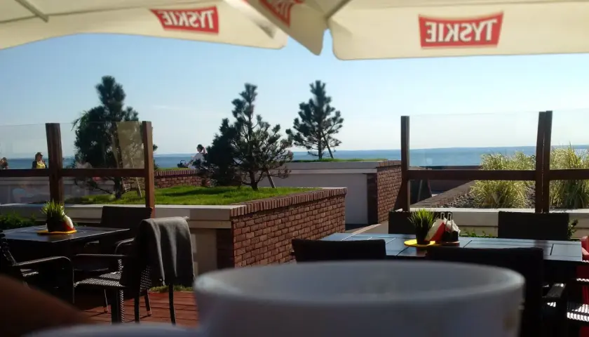 Widok z kawiarni na plaży z widokiem na morze i parasolami z logo Tyskie.